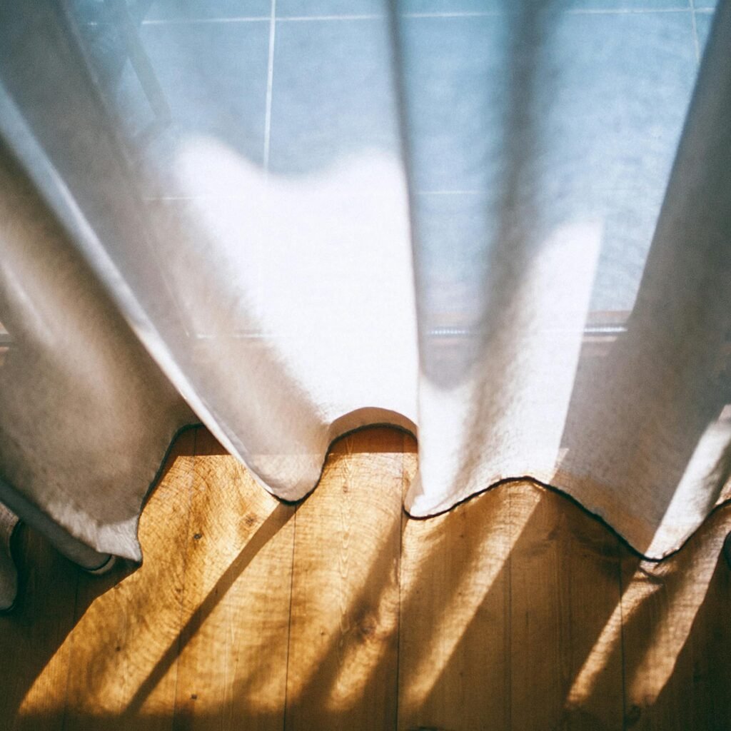 From above of panoramic window with transparent curtains lightened by sunshine in room