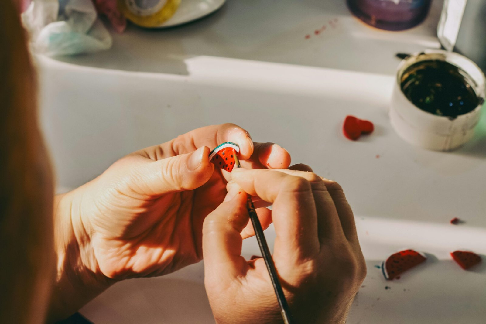 An artistic close-up of a person delicately painting a small strawberry-shaped decoration, highlighting craftsmanship.